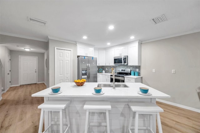 kitchen with a center island with sink, backsplash, a breakfast bar area, white cabinets, and appliances with stainless steel finishes