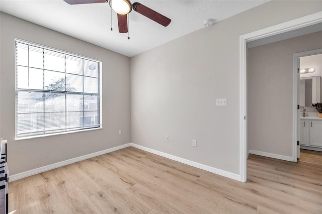 empty room with sink, light wood-type flooring, and ceiling fan