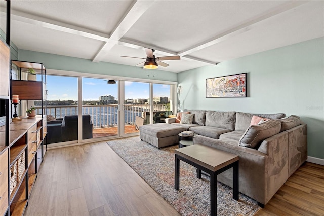 living room with coffered ceiling, a water view, light wood-type flooring, ceiling fan, and beam ceiling