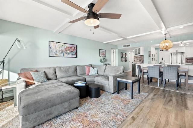 living room with beam ceiling, hardwood / wood-style flooring, and ceiling fan with notable chandelier