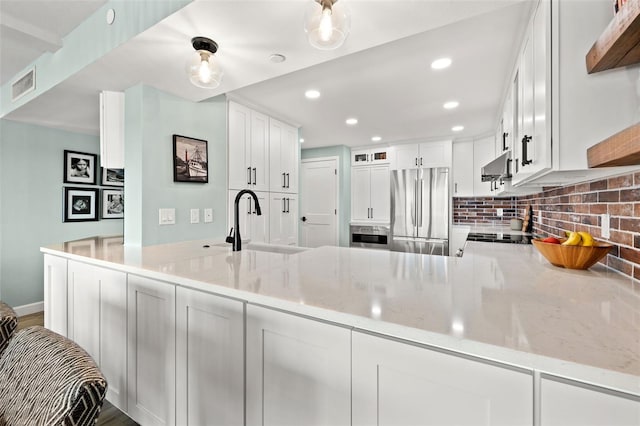 kitchen featuring stainless steel refrigerator, white cabinetry, kitchen peninsula, and light stone counters