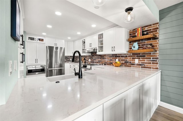 kitchen with white cabinetry, backsplash, light stone countertops, and appliances with stainless steel finishes