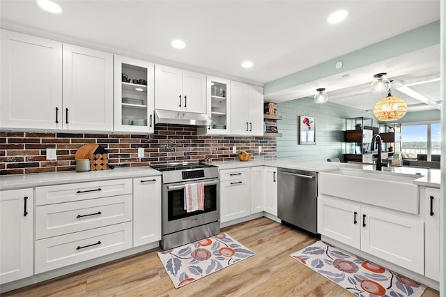 kitchen with appliances with stainless steel finishes, decorative light fixtures, white cabinets, light stone counters, and light hardwood / wood-style flooring