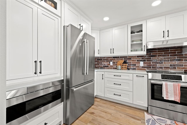 kitchen featuring stainless steel appliances, white cabinets, light wood-type flooring, and decorative backsplash