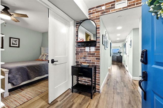 bedroom featuring ceiling fan, brick wall, and hardwood / wood-style floors