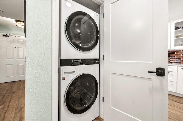 laundry room with stacked washer / dryer and light hardwood / wood-style flooring