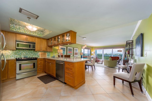 kitchen with light tile patterned floors, appliances with stainless steel finishes, hanging light fixtures, decorative backsplash, and kitchen peninsula