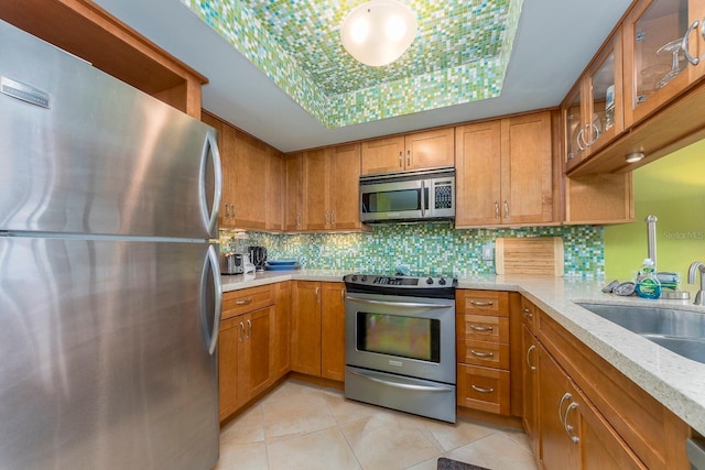 kitchen with appliances with stainless steel finishes, sink, decorative backsplash, light tile patterned floors, and light stone countertops