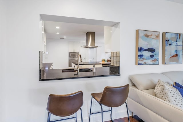 kitchen featuring white cabinetry, island range hood, a breakfast bar area, appliances with stainless steel finishes, and backsplash