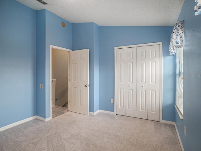 unfurnished bedroom featuring a textured ceiling, light colored carpet, a closet, and lofted ceiling