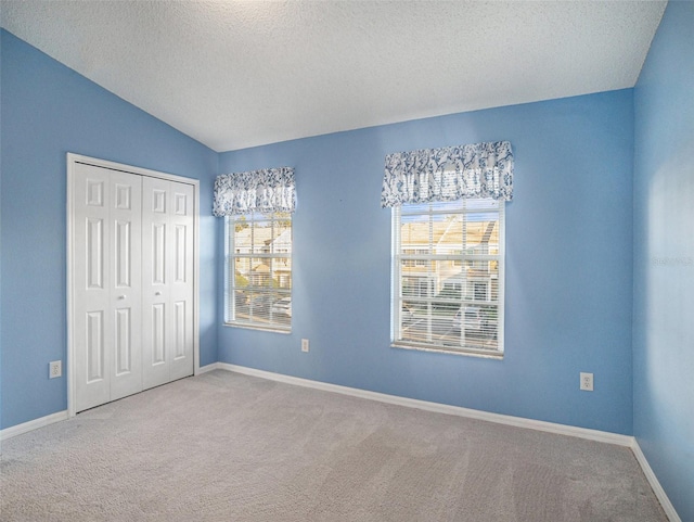 unfurnished bedroom with multiple windows, lofted ceiling, a textured ceiling, and a closet