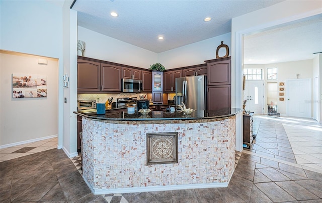 kitchen with appliances with stainless steel finishes, dark brown cabinets, decorative backsplash, and dark stone counters