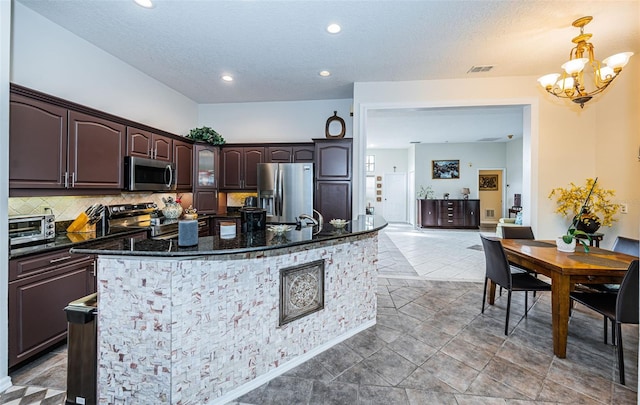 kitchen with dark brown cabinetry, decorative light fixtures, appliances with stainless steel finishes, an island with sink, and backsplash