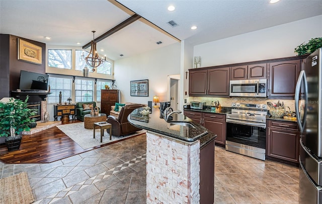 kitchen featuring sink, dark stone counters, hanging light fixtures, stainless steel appliances, and beam ceiling