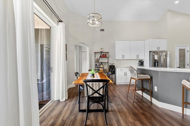 dining area with a towering ceiling, dark wood-style floors, and arched walkways