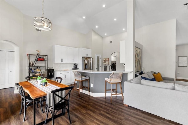 dining area featuring arched walkways, a chandelier, recessed lighting, a towering ceiling, and dark wood finished floors