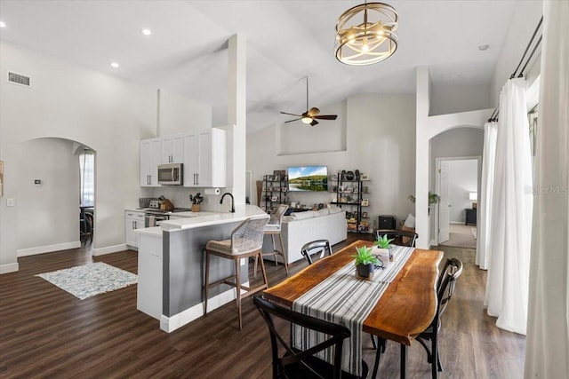 dining space featuring arched walkways, high vaulted ceiling, dark wood finished floors, and visible vents