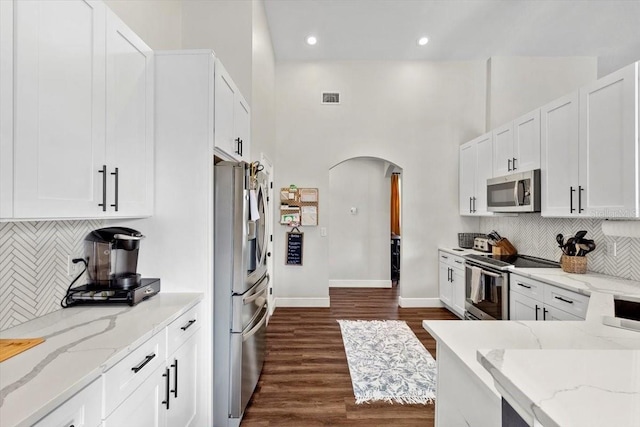 kitchen with arched walkways, visible vents, white cabinets, appliances with stainless steel finishes, and light stone countertops