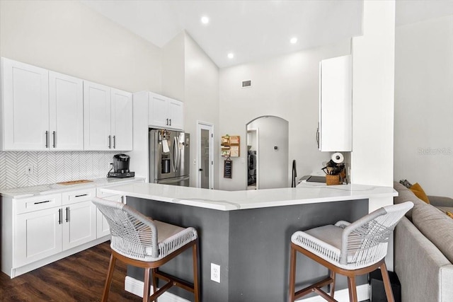 kitchen featuring dark wood-style floors, a breakfast bar, arched walkways, white cabinetry, and stainless steel fridge with ice dispenser