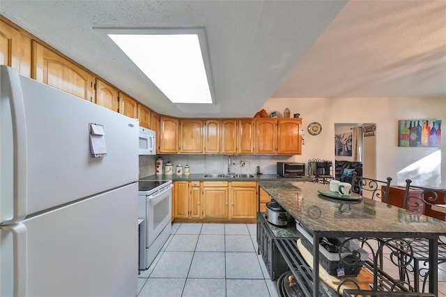 kitchen with a skylight, sink, tasteful backsplash, white appliances, and light tile patterned floors