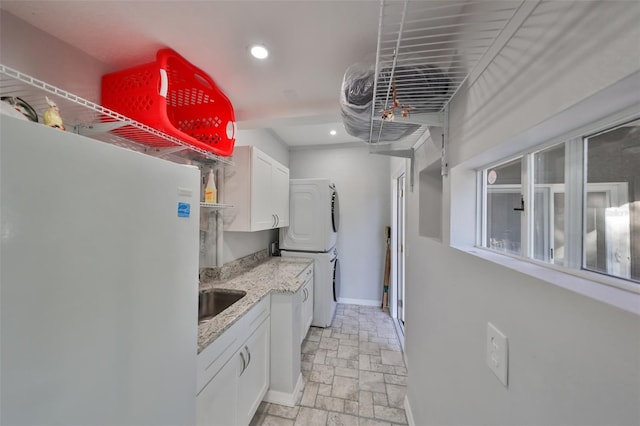 kitchen featuring white fridge, stacked washer and dryer, white cabinetry, and sink