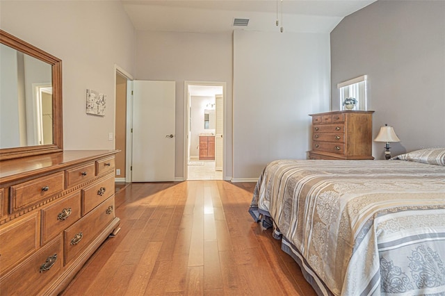 bedroom with connected bathroom, light hardwood / wood-style flooring, and vaulted ceiling