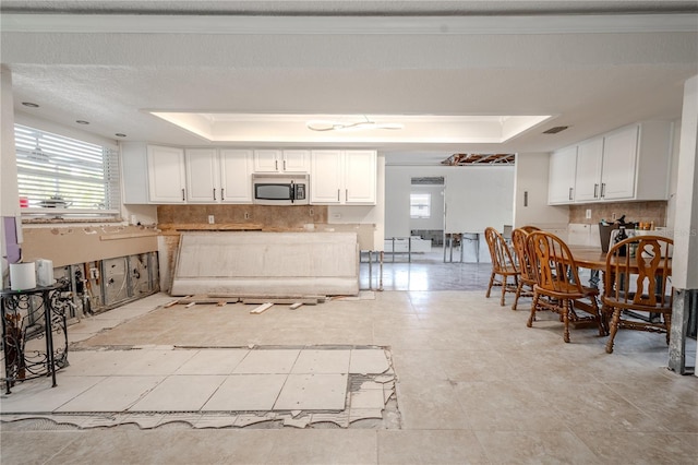 kitchen featuring white cabinets, decorative backsplash, light tile patterned floors, and a tray ceiling