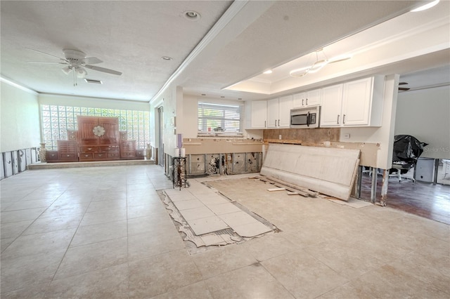 kitchen with a tray ceiling, crown molding, white cabinets, and ceiling fan