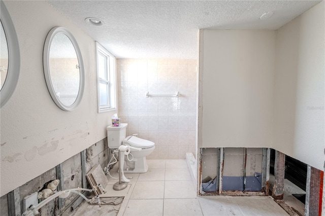 bathroom featuring tile patterned flooring, toilet, tile walls, and a textured ceiling