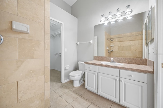 bathroom with toilet, a tile shower, vanity, and tile patterned flooring