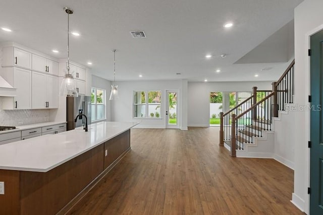 kitchen featuring high end fridge, white cabinetry, decorative light fixtures, and a large island with sink