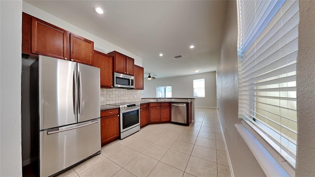 kitchen featuring stainless steel appliances, ceiling fan, light tile patterned floors, kitchen peninsula, and backsplash