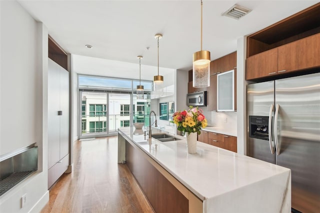 kitchen featuring sink, expansive windows, decorative light fixtures, a center island with sink, and appliances with stainless steel finishes