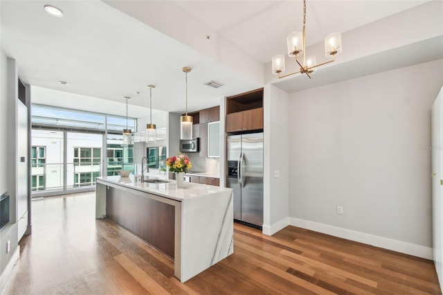 kitchen with a center island with sink, hanging light fixtures, appliances with stainless steel finishes, a wall of windows, and wood-type flooring