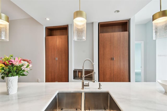 kitchen with light stone counters, sink, and hanging light fixtures