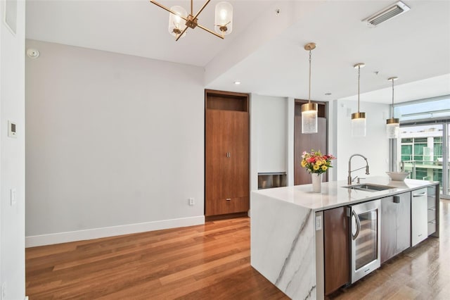 kitchen featuring beverage cooler, sink, pendant lighting, a center island with sink, and hardwood / wood-style flooring