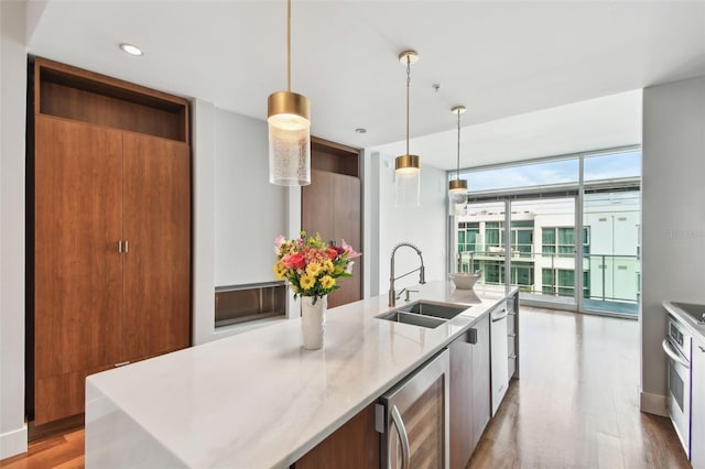 kitchen featuring floor to ceiling windows, a center island with sink, sink, decorative light fixtures, and beverage cooler