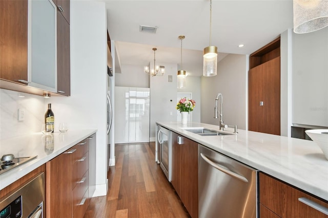 kitchen with light stone countertops, appliances with stainless steel finishes, sink, dark hardwood / wood-style floors, and hanging light fixtures