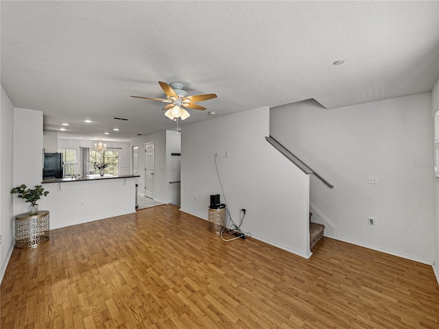 unfurnished living room featuring ceiling fan with notable chandelier, light hardwood / wood-style floors, and a textured ceiling