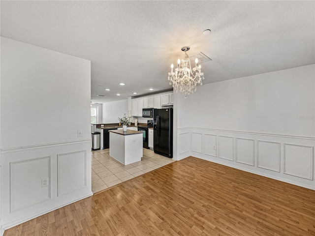 kitchen featuring black appliances, kitchen peninsula, light hardwood / wood-style flooring, white cabinetry, and a chandelier