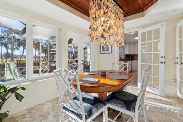 dining space with french doors, a raised ceiling, crown molding, an inviting chandelier, and wooden ceiling