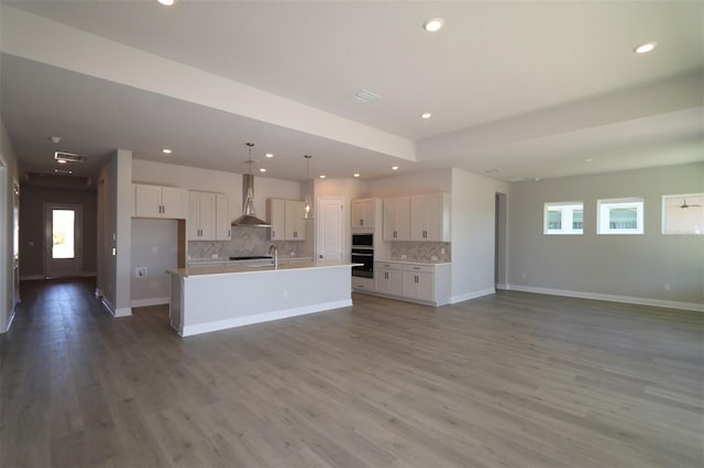 kitchen featuring white cabinets, wall chimney range hood, a kitchen island with sink, and hardwood / wood-style floors