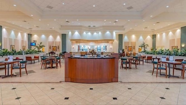 interior space with light tile patterned floors, ornamental molding, a raised ceiling, and a high ceiling