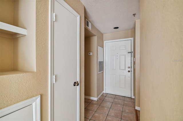 corridor featuring visible vents, baseboards, a textured ceiling, and light tile patterned flooring