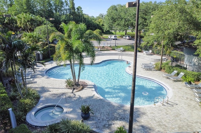 community pool with a patio area, a hot tub, and fence