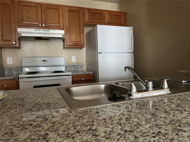 kitchen featuring under cabinet range hood, brown cabinets, white appliances, and a sink