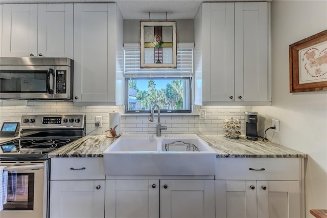 kitchen with light stone countertops, sink, stainless steel appliances, backsplash, and white cabinets