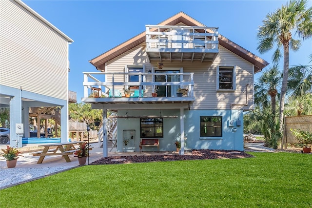 rear view of property featuring a lawn, a balcony, and a patio