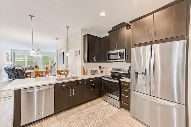 kitchen with kitchen peninsula, hanging light fixtures, sink, stainless steel appliances, and dark brown cabinetry