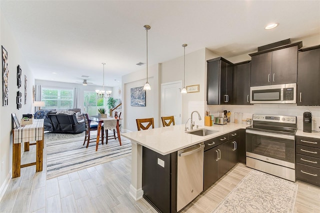 kitchen featuring a notable chandelier, appliances with stainless steel finishes, sink, kitchen peninsula, and pendant lighting